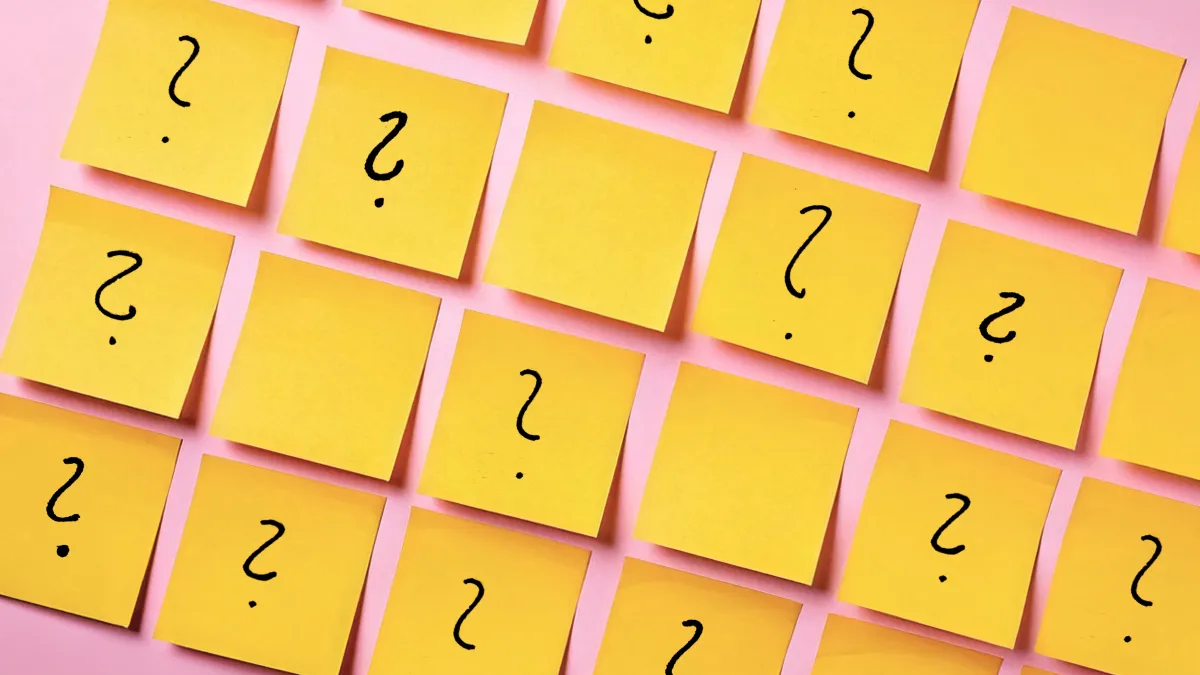 Mehrere gelbe Post-it-Notizen mit Fragezeichen sind symmetrisch auf einem rosa Hintergrund angeordnet